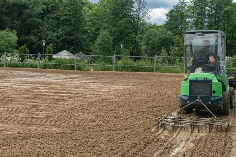 Compact green mini loader tractor levelling sand soil with drag harrow harr.. Stock Photos