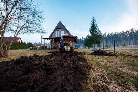 Compact loader carves muddy ruts toward steep roof A frame house at dusk Stock Photos