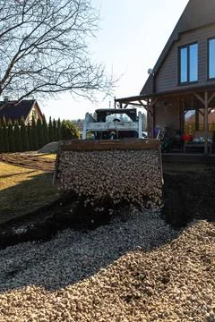 Compact loader pours crushed stone beside modern wood clad house Stock Photos