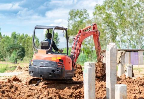 Compact orange mini excavator digging soil at a rural construction site dur.. Stock Photos