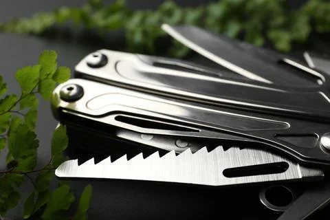 Compact portable metallic multitool and green leaves on black background, clo Stock Photos