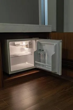 A compact refrigerator stands open in a dark hotel room with only its inner.. Foto stock