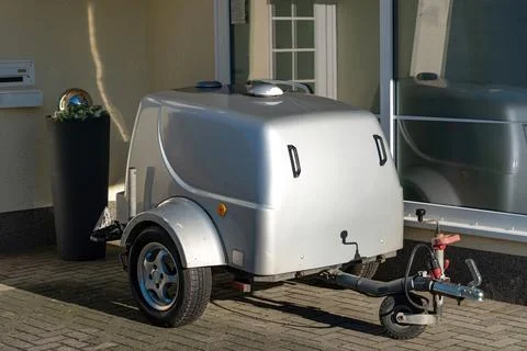 Compact silver trailer parked outside a building during daylight Stock Photos