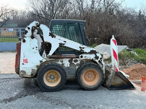 Compact skid steer loader parked on asphalt near roadwork barriers and constr Stock Photos