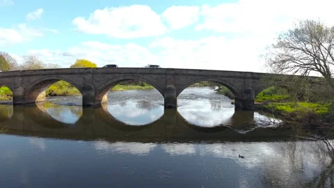 Compact SUV moving along old masonry bridge above slow river with tree Stock Footage 340326198