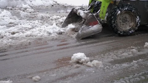 A compact tractor with a scoop removing slush and snow from a parking area. Stock Footage 327275529