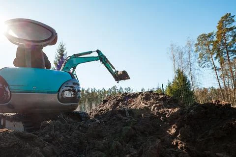 Compact turquoise excavator digs at forest edge in dawn light Stock-Fotos