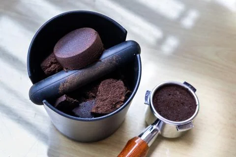 Compacted coffee ground in knock box with portafilter next to it. Coffee grounds Stock Photos