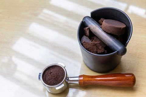 Compacted coffee ground in knock box with portafilter next to it. Coffee grounds Foto stock