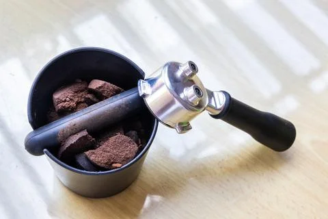 Compacted coffee ground in knock box with portafilter next to it. Coffee grounds Foto stock