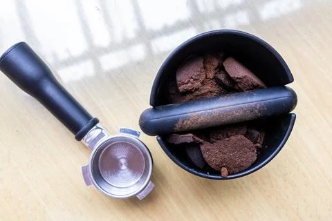Compacted coffee ground in knock box with portafilter next to it. Coffee grounds Stock Photos