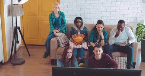 Company of friends is playing on a computer console. Sitting on the sofa and on Vídeo Stock 88656966