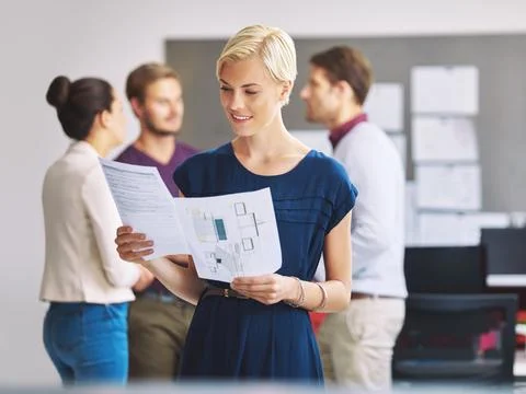 Comparing notes. a young female designer looking over some paperwork with her Stock Photos