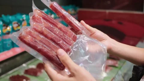 Comparing two packs of row organic meat sausages in vacuum packages held in Stock Footage 166691850
