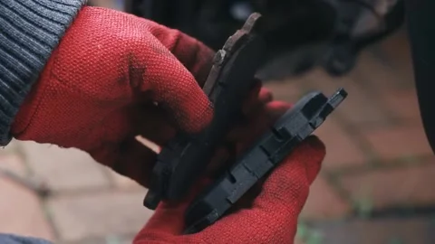 Comparing worn brake pad with new replacement component in gloved hands Stock Footage 341568821