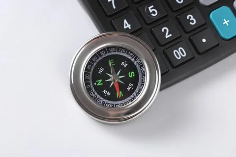 Compass and calculator on white surface for navigation and finance Stock Photos