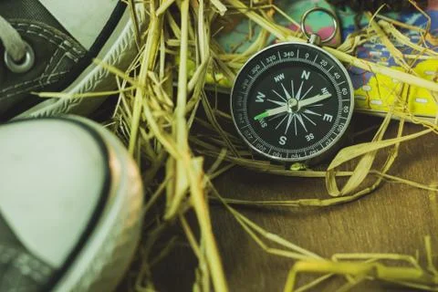Compass and paper maps with sneaker and pine flower placed on dry wheat straw. Foto stock