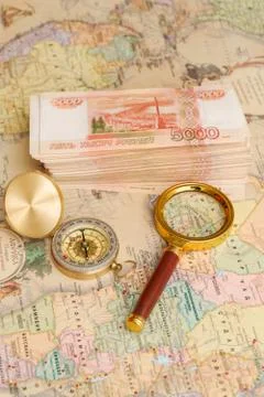 A compass with a bundle of big money and a magnifying glass are on the map Stock Photos