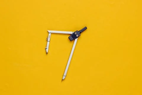 Compass for drawing on yellow background. Top view. Stationery. Engineering Stockfoto's