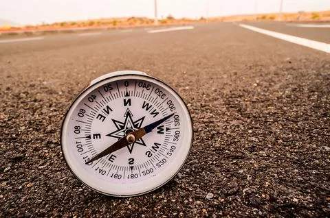 A compass is laying on the ground in front of a road Stock Photos