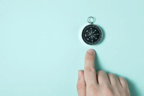 Compass on light blue background. The index finger points to the compass. Foto stock