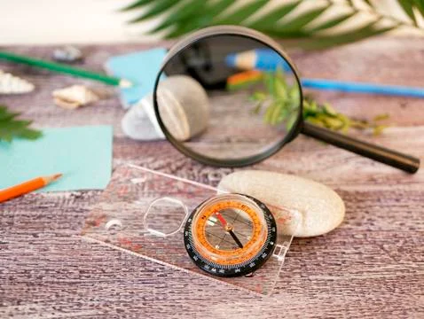 Compass, magnifier, notepad, pencil, sea stones, palm leaf Stock Photos