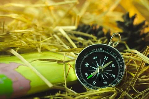 Compass with paper maps and pine flowers placed on dry wheat straw. Stock Photos
