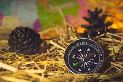 Compass with paper maps and pine flowers placed on dry wheat straw in morning. Stock Photos