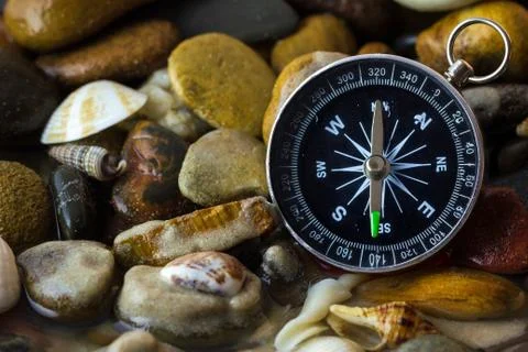 Compass on the pebbles and shell at riverside. Stock Photos