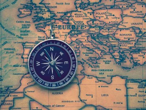 The compass is placed on the ancient or vintage world map between Europe co.. Stock Photos