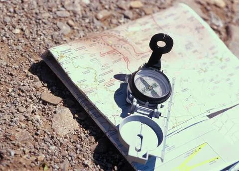 Compass resting on open map surrounded by gravel on a sunny day outdoors Stock Photos