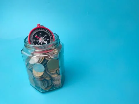 A compass sits at the top opening of a clear glass jar filled with mixed co.. 库存照片