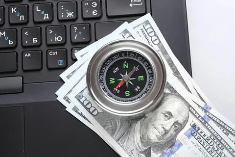 Compass on us dollar bills next to a computer keyboard Stock Photos