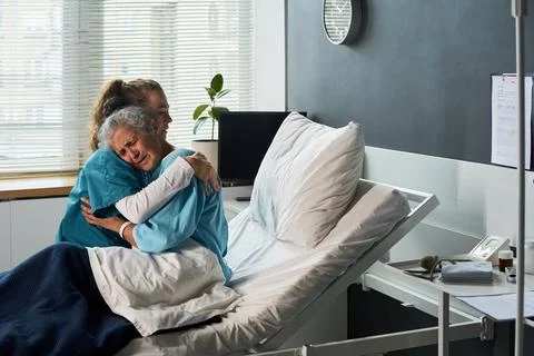Compassionate Nurse Hugging Crying Senior Patient in Hospital Room Stock Photos