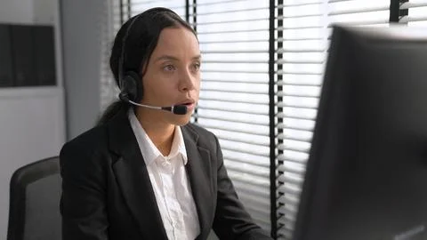 Competent female operator working on computer and while talking with clients. Foto stock