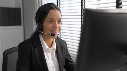 Competent female operator working on computer and while talking with clients. Foto stock