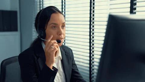 Competent female operator working on computer and while talking with clients. Foto stock