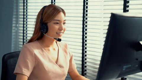 Competent female operator working on computer and while talking with clients. Foto stock