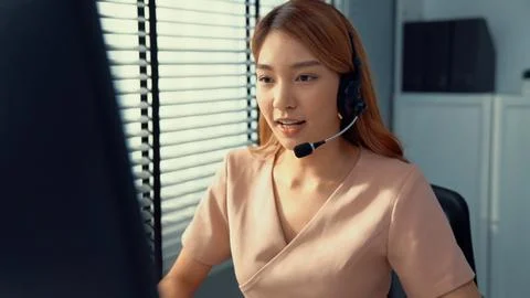 Competent female operator working on computer and while talking with clients. Foto stock