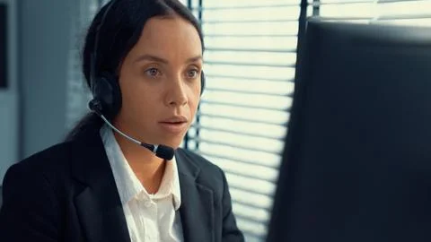 Competent female operator working on computer and while talking with clients. Foto stock