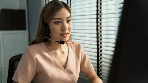 Competent female operator working on computer and while talking with clients. Foto stock