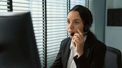 Competent female operator working on computer and while talking with clients. Foto stock