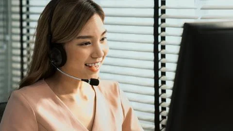 Competent female operator working on computer and while talking with clients. Foto stock