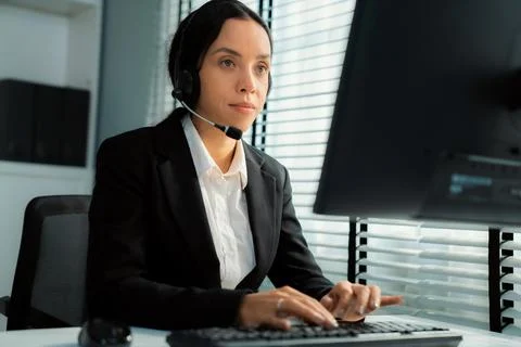 Competent female operator working on computer and while talking with clients. Foto stock