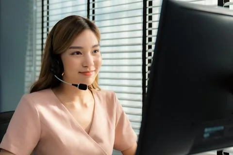 Competent female operator working on computer and while talking with clients. Foto stock