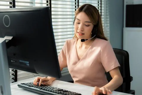 Competent female operator working on computer and while talking with clients. Foto stock