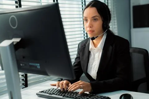 Competent female operator working on computer and while talking with clients. Foto stock