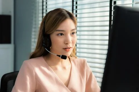 Competent female operator working on computer and while talking with clients. Foto stock