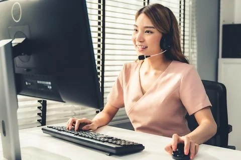 Competent female operator working on computer and while talking with clients. Foto stock