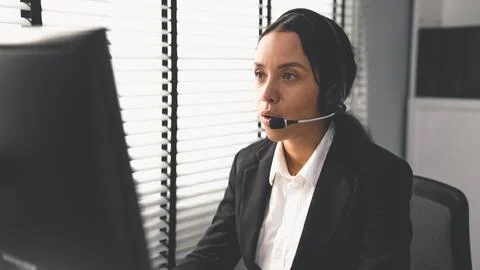 Competent female operator working on computer and while talking with clients. Foto stock